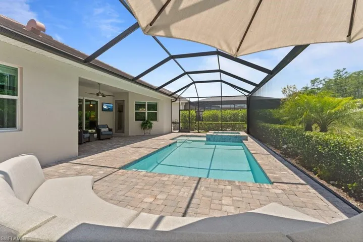View of pool featuring a patio, ceiling fan, a pool with connected hot tub, and glass enclosure