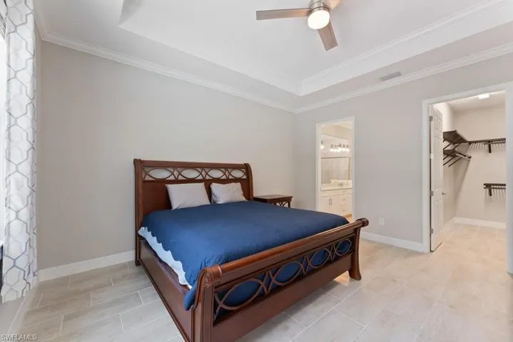 Bedroom with a raised ceiling, crown molding, ensuite bath, ceiling fan, and baseboards