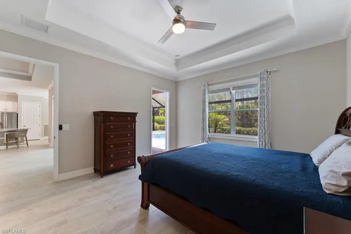 Bedroom with a raised ceiling, crown molding, stainless steel fridge with ice dispenser, and ceiling fan