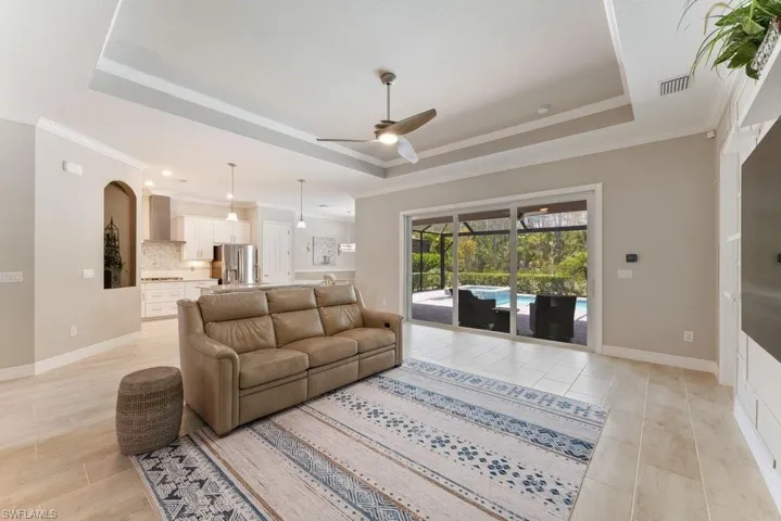 Living area with a tray ceiling, a ceiling fan, ornamental molding, light tile patterned floors, and recessed lighting