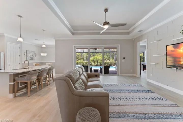 Living area with a ceiling fan, crown molding, a tray ceiling, light wood-type flooring, and baseboards