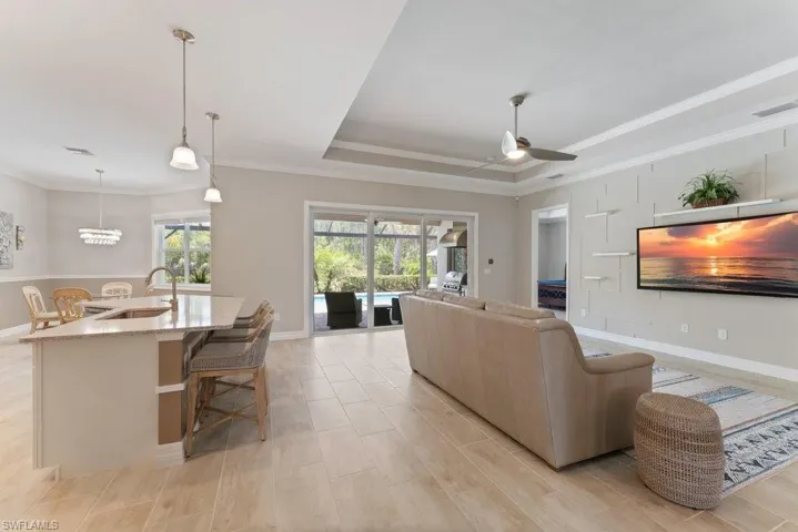 Living area featuring a raised ceiling, a ceiling fan, crown molding, baseboards, and light wood-type flooring