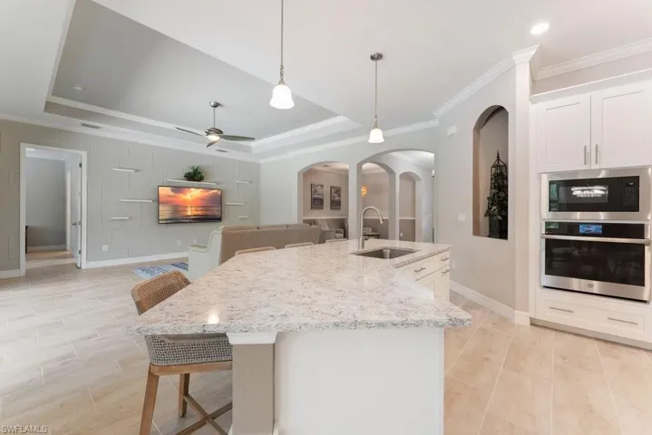 Kitchen with stainless steel appliances, a sink, a tray ceiling, crown molding, and arched walkways