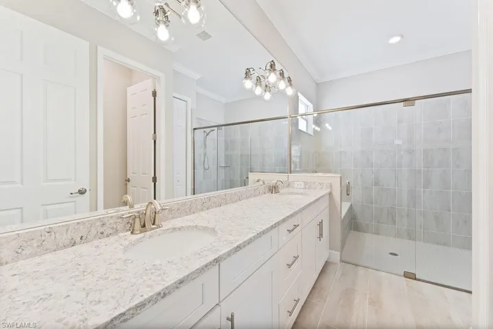 Full bathroom with double vanity, a tile shower, crown molding, and a bath