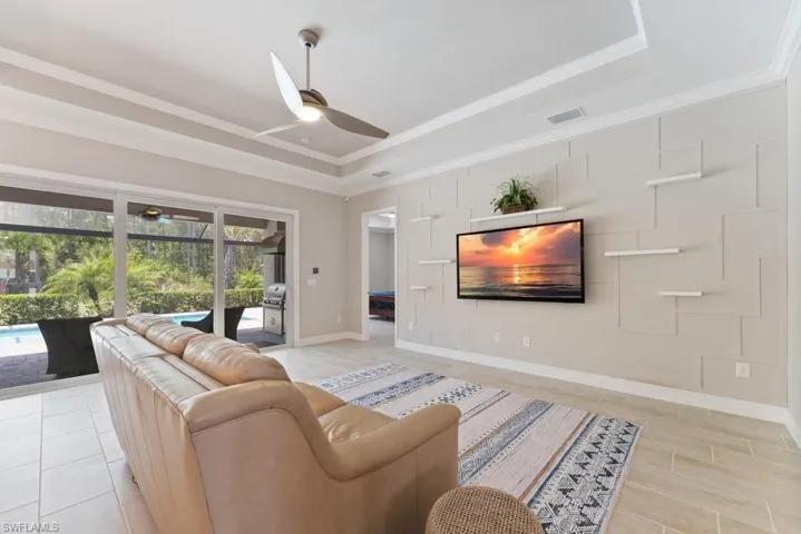 Living room with a ceiling fan, a raised ceiling, healthy amount of natural light, and crown molding