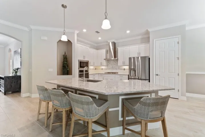 Kitchen with stainless steel appliances, a sink, wall chimney exhaust hood, arched walkways, and baseboards