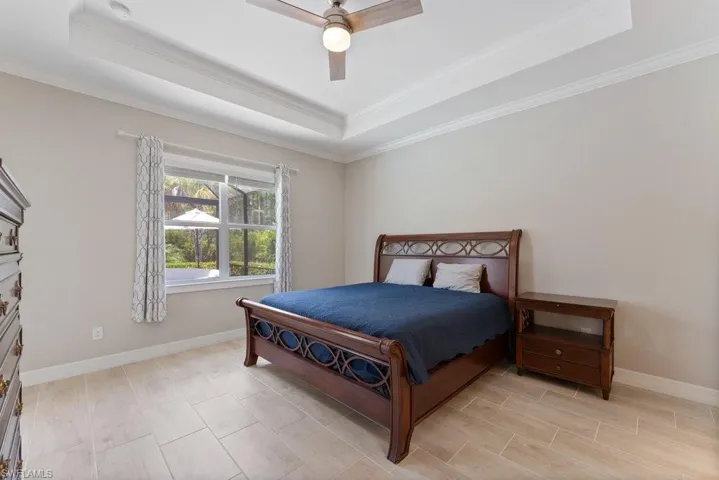 Bedroom featuring a raised ceiling, crown molding, baseboards, and ceiling fan