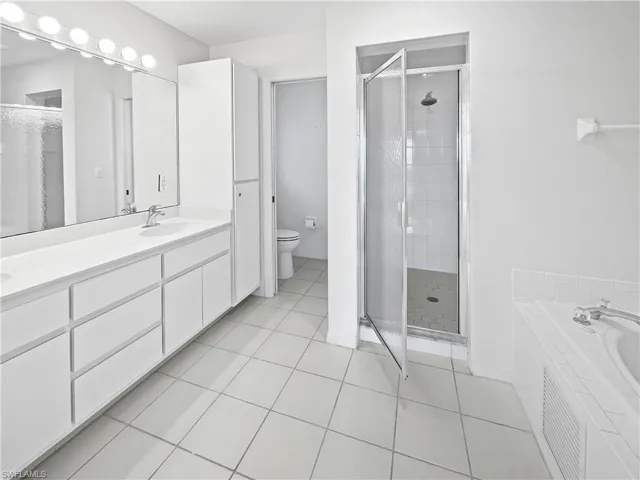 Master Bathroom with double vanity, a shower stall, light tile patterned flooring, and a garden tub