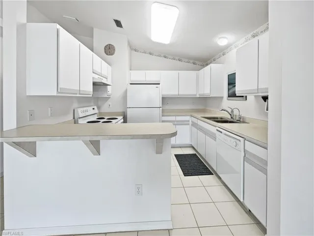 Kitchen featuring a kitchen bar, white cabinets, white appliances, lofted ceiling, and light countertops