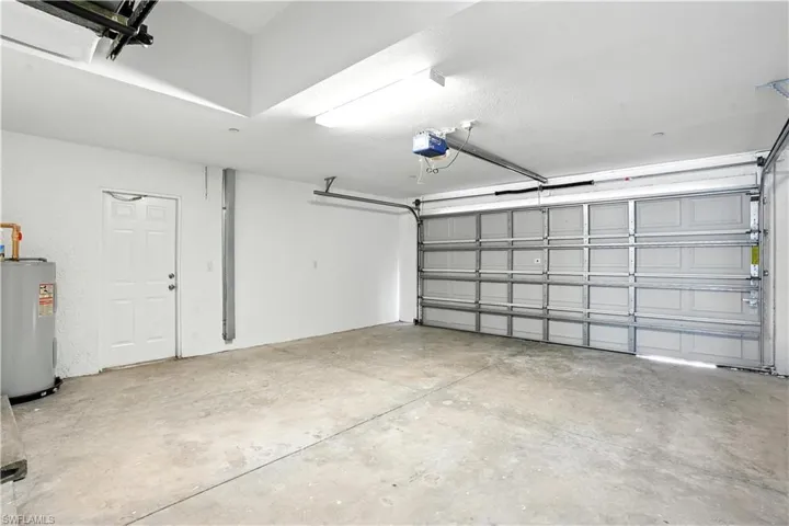 Spacious garage featuring a concrete floor, overhead lighting, a white interior door, a water heater, and an automatic garage door opener