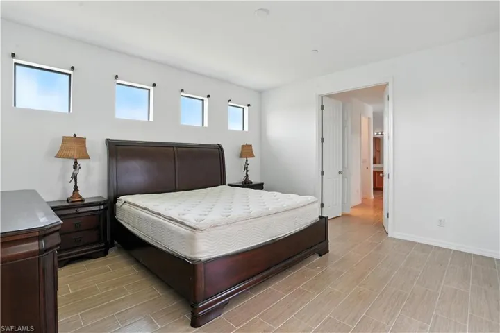 Spacious bedroom featuring light-toned tile flooring, white walls, and a series of high-set rectangular windows