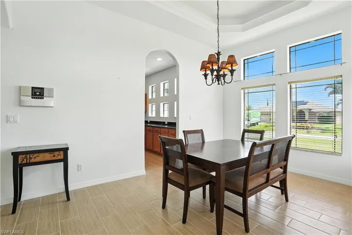 Dining area featuring high tray ceilings, a chandelier with decorative shades, large windows with horizontal blinds, and tile flooring