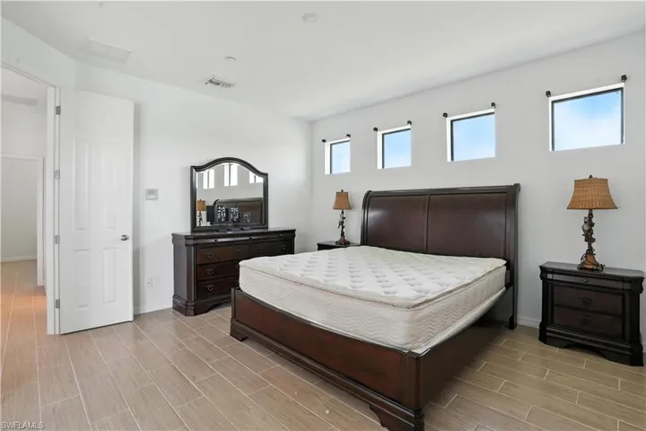 Spacious bedroom featuring light wood-finish tile flooring, crisp white walls, and four high-set windows