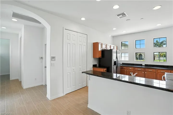 Bright kitchen featuring recessed lighting, a black appliance suite, wood cabinetry, dark countertops, and multiple windows