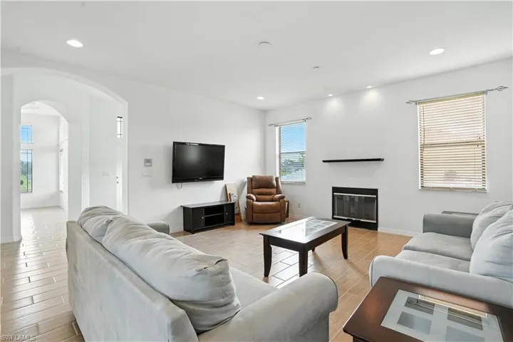 Living area featuring wood-finish flooring, a fireplace with a black mantel, recessed lighting, and an arched entryway