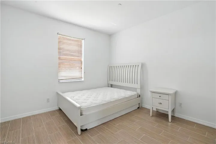 Bedroom featuring wood-finish tile flooring, white baseboards, a window with horizontal blinds, and clean white walls