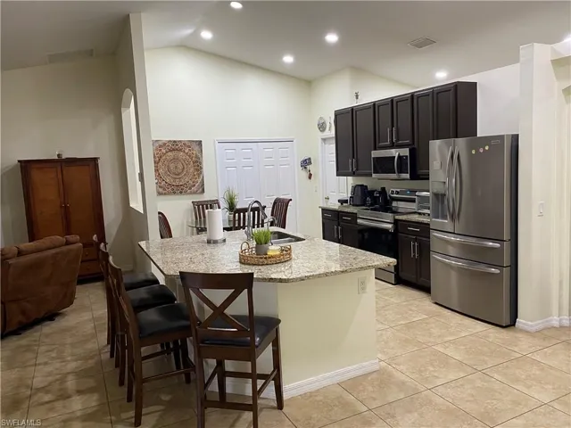Kitchen with visible vents, a breakfast bar, a kitchen island with sink, stainless steel appliances, and light tile patterned floors