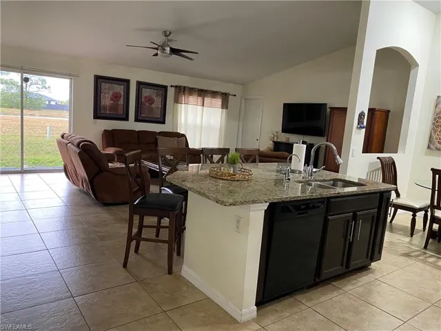 Kitchen featuring a kitchen island with sink, a sink, open floor plan, dishwasher, and vaulted ceiling