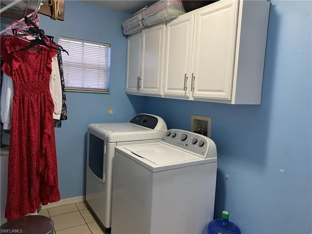 Laundry area with washing machine and clothes dryer, light tile patterned floors, cabinet space, and baseboards