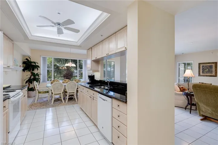 Kitchen with a raised ceiling, white appliances, light tile patterned floors, healthy amount of natural light, and crown molding