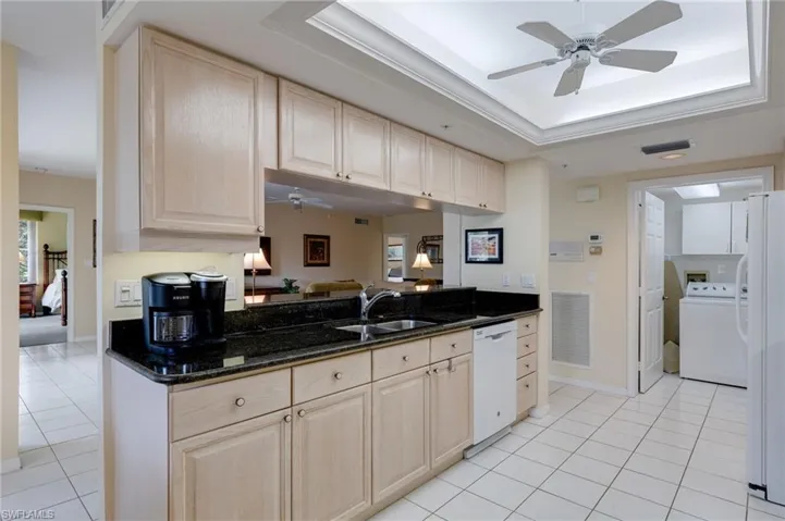 Kitchen featuring ceiling fan, a tray ceiling, dark stone countertops, washer / clothes dryer, and light tile patterned flooring