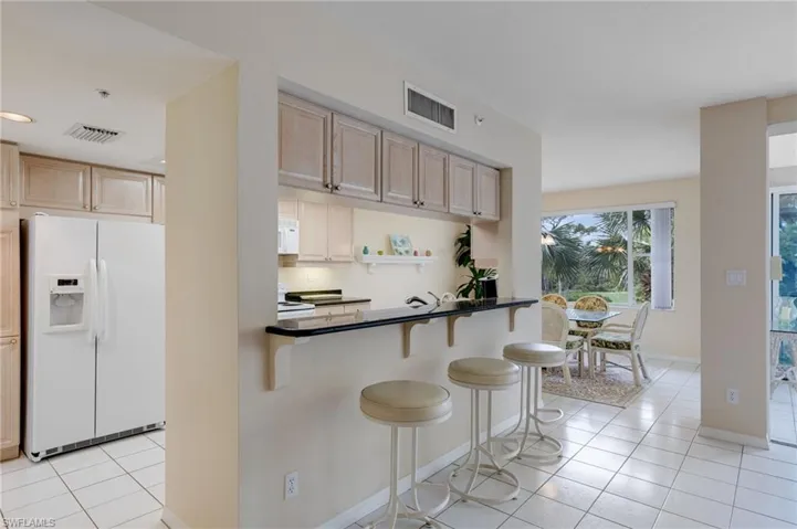 Kitchen with light tile patterned floors, white appliances, light brown cabinets, a breakfast bar, and open shelves