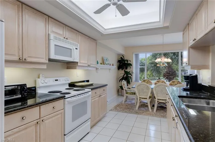 Kitchen with white appliances, a tray ceiling, light tile patterned floors, pendant lighting, and dark stone counters
