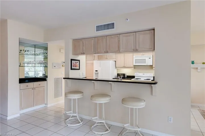 Kitchen with dark countertops, white appliances, light tile patterned flooring, a kitchen breakfast bar, and light brown cabinetry