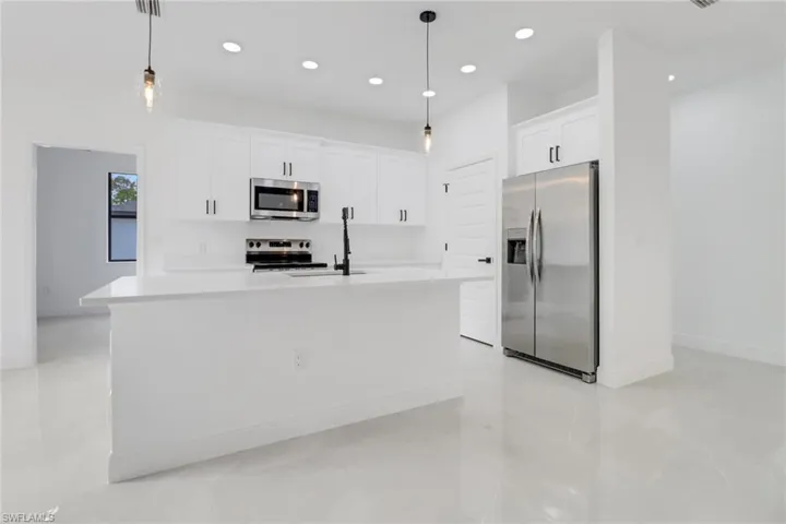 Kitchen with white cabinetry, pendant lighting, stainless steel appliances, and a kitchen island with sink