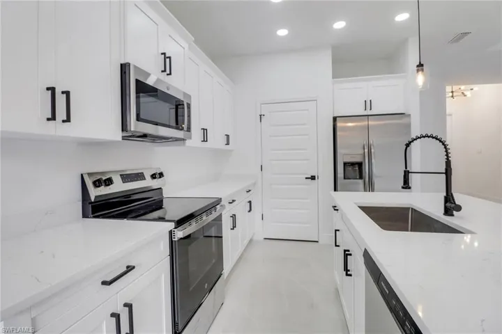 Kitchen with appliances with stainless steel finishes, sink, decorative light fixtures, white cabinets, and light stone counters