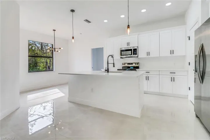 Kitchen with pendant lighting, sink, white cabinets, a center island with sink, and stainless steel appliances