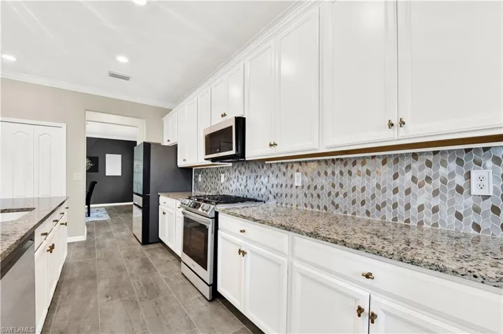 Kitchen featuring white cabinetry, ornamental molding, stainless steel appliances, light stone counters, and tasteful backsplash