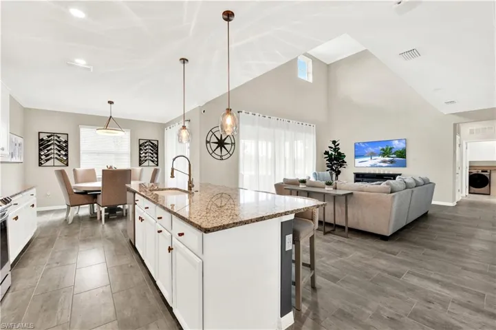 Kitchen with washer / clothes dryer, a kitchen breakfast bar, white cabinetry, an island with sink, and sink