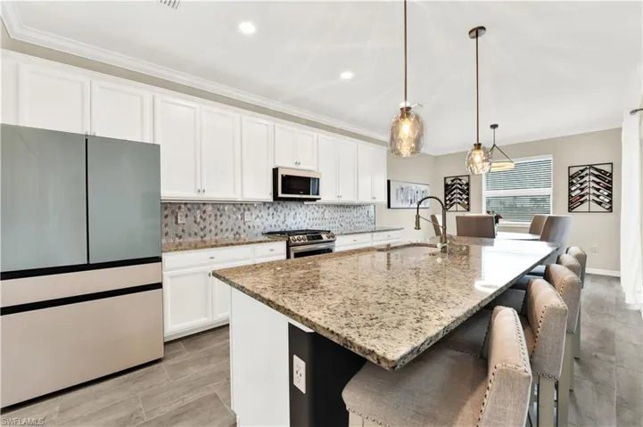 Kitchen with an island with sink, white cabinets, decorative light fixtures, and appliances with stainless steel finishes