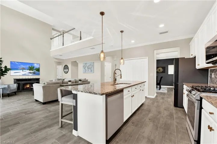 Kitchen featuring a center island with sink, stainless steel appliances, light stone counters, sink, and white cabinetry