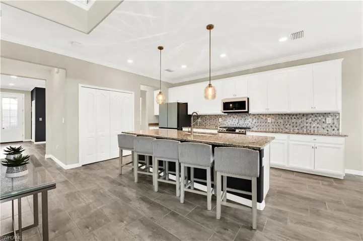 Kitchen with white cabinets, stainless steel appliances, backsplash, an island with sink, and sink