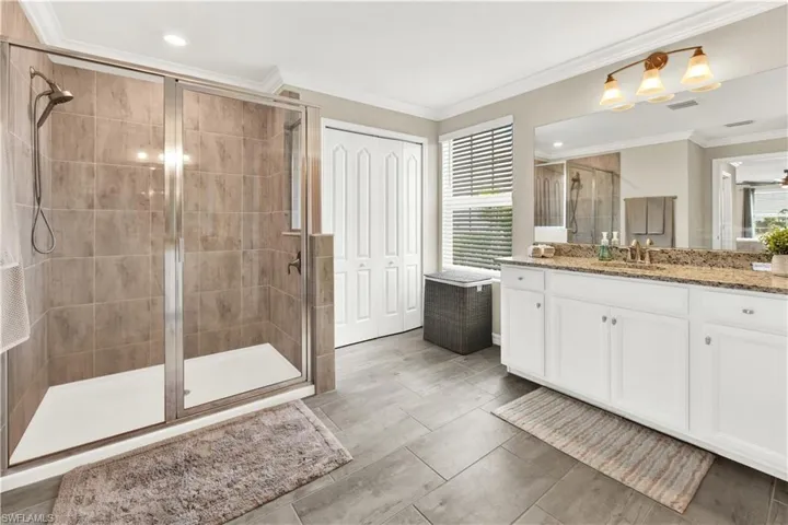 Bathroom featuring crown molding, a shower with door, and vanity
