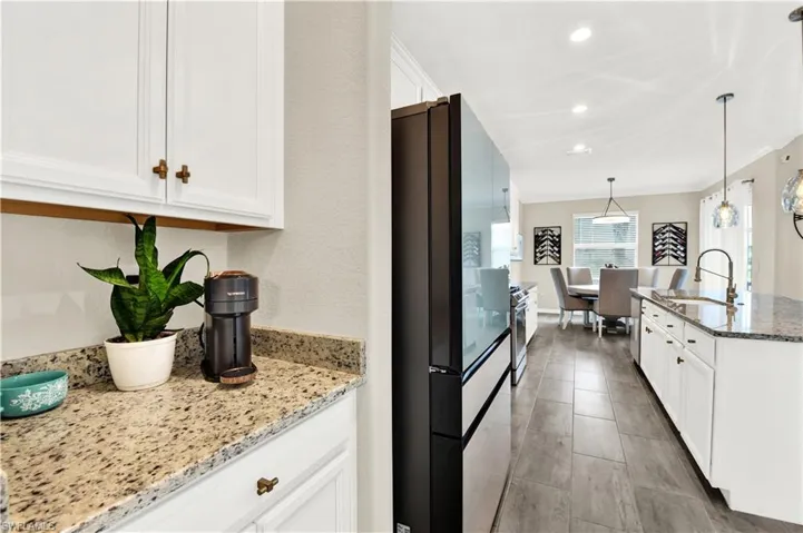 Kitchen featuring black fridge, white cabinetry, hanging light fixtures, light stone counters, and sink