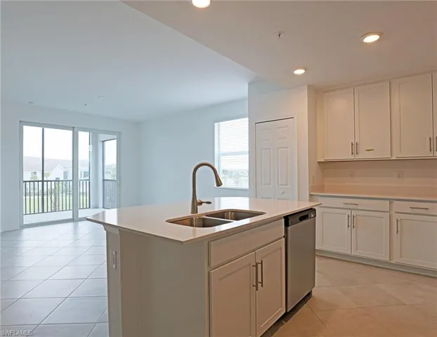Kitchen featuring light tile patterned flooring, stainless steel dishwasher, a kitchen island with sink, recessed lighting, and white cabinetry