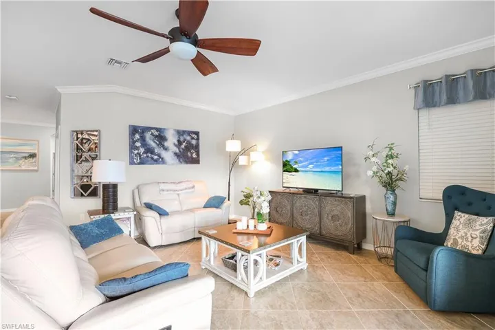 Tiled living room with ceiling fan and ornamental molding