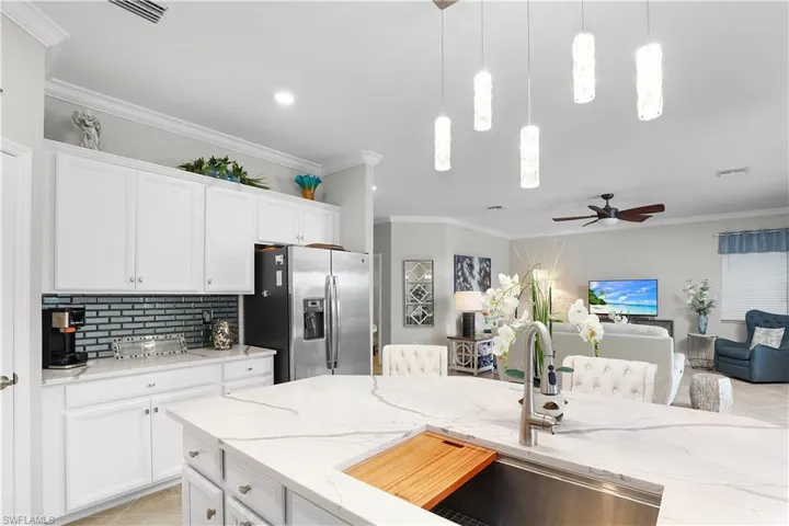 Kitchen with pendant lighting, white cabinetry, light stone counters, ceiling fan, and stainless steel refrigerator with ice dispenser