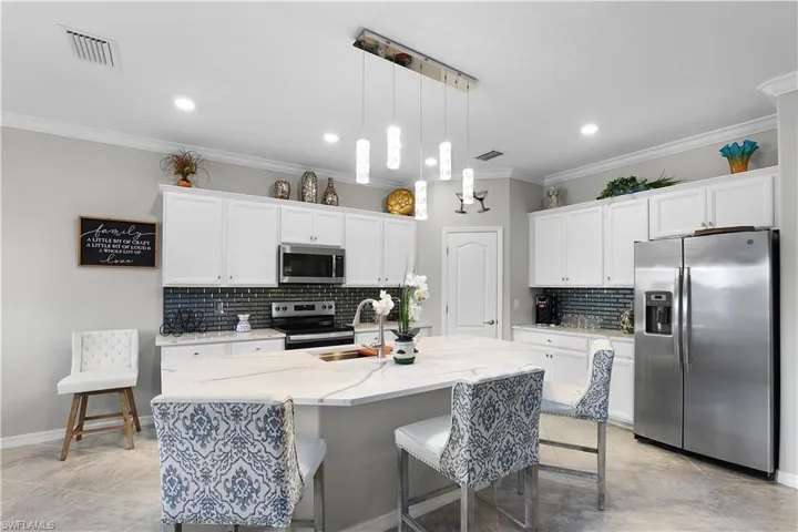 Kitchen with a kitchen island with sink, appliances with stainless steel finishes, sink, backsplash, and decorative light fixtures