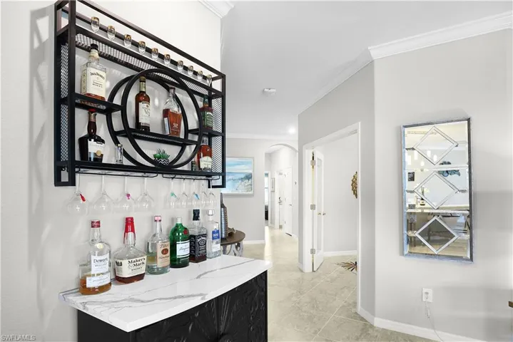 Bar featuring light stone countertops, crown molding, and light tile patterned floors