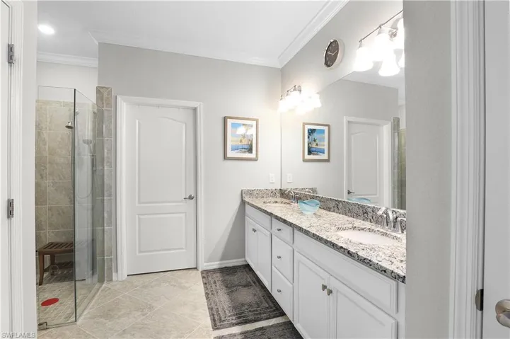 Bathroom with a shower with shower door, tile patterned floors, dual bowl vanity, and ornamental molding