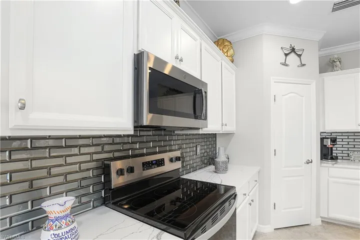 Kitchen with crown molding, decorative backsplash, appliances with stainless steel finishes, white cabinetry, and light stone counters