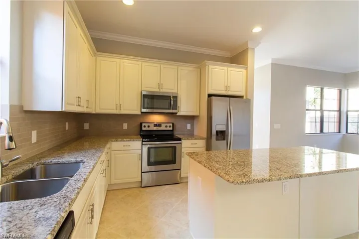 Kitchen with a sink, tasteful backsplash, light stone countertops, a center island, and stainless steel appliances