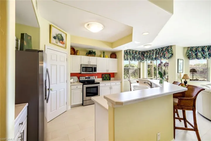 Kitchen featuring stainless steel appliances, a kitchen island with sink, light countertops, a breakfast bar, and white cabinets