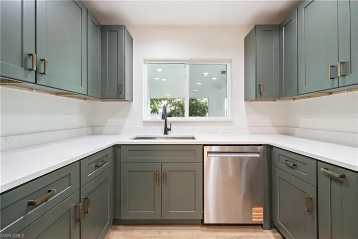 Kitchen featuring stainless steel dishwasher, light stone countertops, light wood-style floors, and green cabinetry