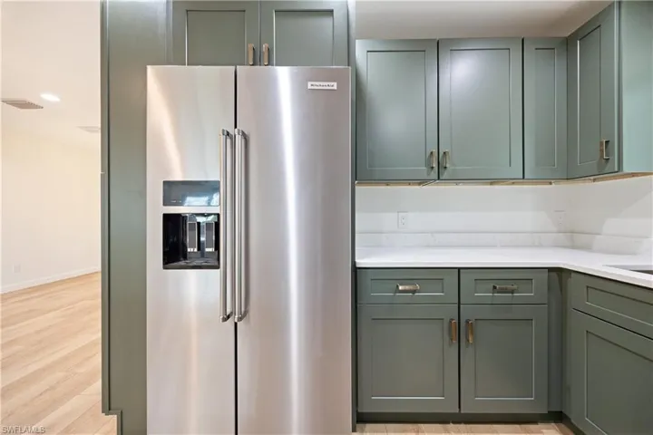 Kitchen with high quality fridge, light wood-style floors, green cabinetry, recessed lighting, and light stone counters