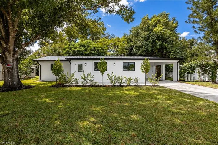 Ranch-style home featuring a metal roof, a front lawn, driveway, a carport, and view of wooded area